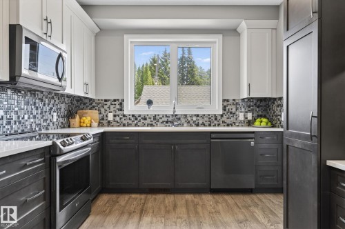 Modern kitchen featuring two-tone cabinetry, stainless steel appliances, a mosaic tile backsplash, wood-finish flooring, and a window above the sink - 8809 148 Street, Edmonton, AB - Indoor Photo Showing Kitchen With Upgraded Kitchen
