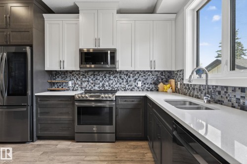 Contemporary kitchen featuring two-tone cabinetry, stainless steel appliances, a mosaic tile backsplash, and light-toned countertops - 8809 148 Street, Edmonton, AB - Indoor Photo Showing Kitchen With Double Sink With Upgraded Kitchen