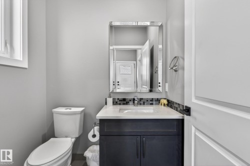 Powder room featuring a dark wood vanity with a white countertop, mosaic tile backsplash, and a contemporary mirror - 8809 148 Street, Edmonton, AB - Indoor Photo Showing Bathroom