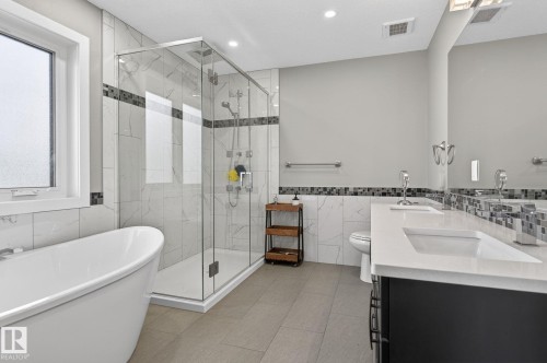 Modern bathroom featuring a freestanding soaking tub, a frameless glass shower enclosure, a dual-sink vanity with a light-toned countertop, and a mosaic tile backsplash - 8809 148 Street, Edmonton, AB - Indoor Photo Showing Bathroom