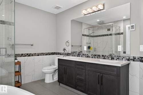 Contemporary bathroom featuring a dark wood double vanity with dual sinks, a large wall-mounted mirror, and a frameless glass-enclosed shower - 8809 148 Street, Edmonton, AB - Indoor Photo Showing Bathroom