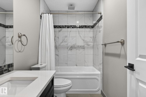 Bathroom featuring a built-in tub with shower, white and gray marbled wall tiles, decorative mosaic accent tile, white countertop with integrated sink, and dark wood-finish vanity - 8809 148 Street, Edmonton, AB - Indoor Photo Showing Bathroom