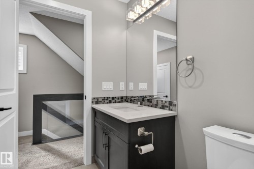 Powder room featuring a dark wood-finish vanity with an integrated sink, a tiled backsplash, and a contemporary light fixture - 8809 148 Street, Edmonton, AB - Indoor Photo Showing Bathroom