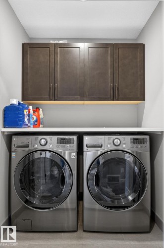 Dedicated laundry area featuring a white countertop, built-in dark wood-finish cabinetry with linear hardware, and light gray tiled flooring - 8809 148 Street, Edmonton, AB - Indoor Photo Showing Laundry Room