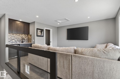 Open concept bonus room with a wet bar featuring dark cabinetry, a mosaic tile backsplash, and a stainless steel sink - 8809 148 Street, Edmonton, AB - Indoor Photo Showing Other Room