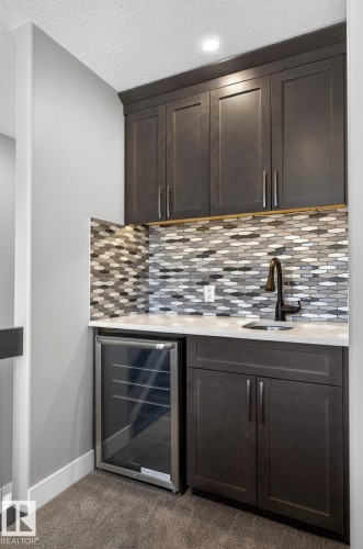 Wet bar with dark wood-finish cabinetry, a patterned tile backsplash, white countertop, and under-counter beverage refrigerator - 8809 148 Street, Edmonton, AB - Indoor