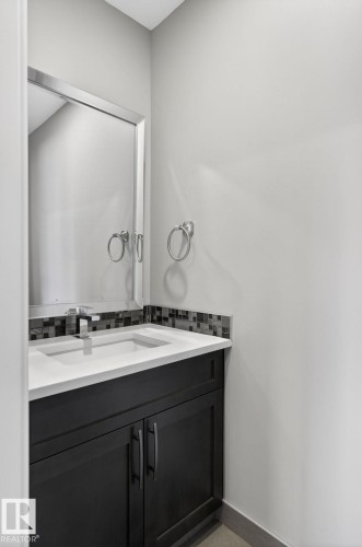 Contemporary vanity featuring a dark wood finish, a white countertop with an integrated sink, and a multi-toned mosaic tile backsplash - 8809 148 Street, Edmonton, AB - Indoor Photo Showing Bathroom