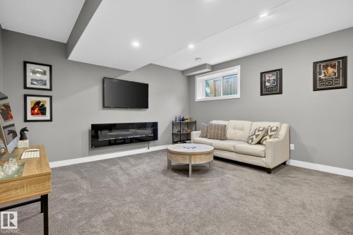 Finished living area featuring gray carpet, recessed lighting, and a wall-mounted electric fireplace - 8809 148 Street, Edmonton, AB - Indoor Photo Showing Other Room With Fireplace