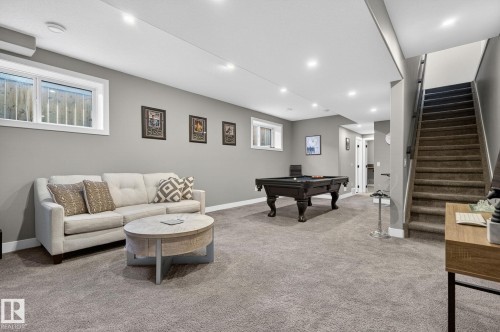 Carpeted recreation room featuring recessed lighting, a built-in air conditioning unit, and a carpeted staircase with a dark wood-finish handrail - 8809 148 Street, Edmonton, AB - Indoor