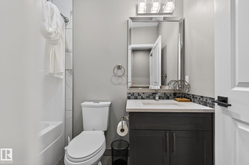 Bathroom featuring a dark gray vanity with a light countertop, a mosaic tile backsplash, and a mirrored vanity light fixture - 8809 148 Street, Edmonton, AB - Indoor Photo Showing Bathroom
