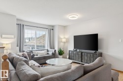Spacious living area featuring light wood-finish flooring, a contemporary ceiling light fixture, large window with curtains, and neutral wall tones - 