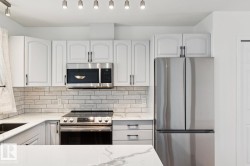 Kitchen featuring white cabinetry with dark hardware, a stainless steel electric range, an over-the-range microwave, a stainless steel refrigerator, and light-toned subway tile backsplash - 