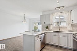Modern kitchen featuring white cabinetry, light-toned countertops, a subway tile backsplash, and stainless steel appliances - 