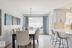 Bright dining area featuring a modern chandelier, light wood-finish flooring, and a window with blinds - 