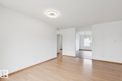 Spacious room featuring light wood-finish flooring, white painted walls, and a modern ceiling light fixture - 