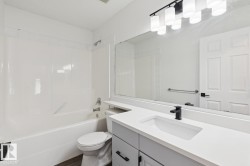 Bathroom featuring a white bathtub with an integrated shower, a toilet, and wood-finish flooring - 