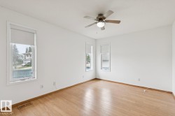 Bright room featuring wood-finish flooring, white walls, and a ceiling fan with integrated lighting - 