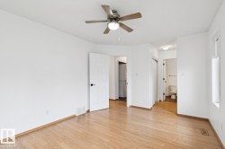 Spacious room featuring wood-finish flooring, a ceiling fan with integrated lighting, and crisp white walls - 