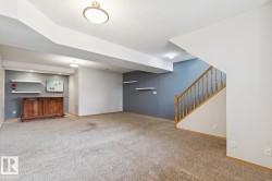 Spacious carpeted room featuring a built-in wooden bar, recessed lighting, floating wall shelves, and a wooden staircase with balusters - 