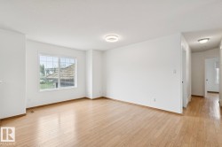 Bright open room featuring wood-finish flooring, white walls, a large window with grid pattern, and a modern flush-mount ceiling light - 