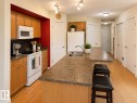 Functional kitchen featuring an eat-at island, dual-basin stainless steel sink, wood-finish cabinetry, built-in microwave, and wood-finish flooring - 102 Hartwick Loop, Spruce Grove, AB 