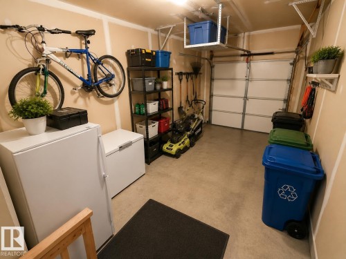 Spacious garage featuring a concrete floor, overhead storage rack, and a segmented garage door - 102 Hartwick Loop, Spruce Grove, AB 