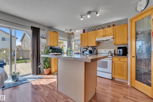 Kitchen featuring wood-finish flooring, light wood cabinetry, a center island with a light-toned countertop, and sliding glass patio doors opening to a wood deck - 14031 136 Street, Edmonton, AB 