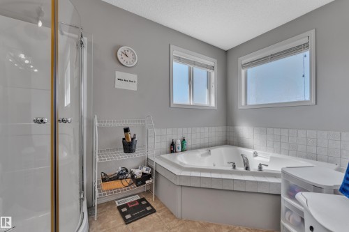 Corner jetted tub with tile surround, two windows, and an adjacent enclosed shower - 14031 136 Street, Edmonton, AB 