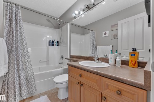 Bathroom featuring a built-in bathtub with shower, wood-finish vanity with an integrated sink, broad mirror, and tiled flooring - 14031 136 Street, Edmonton, AB 