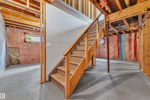 Unfinished basement showcasing structural wood framing, concrete flooring, and an exposed wooden staircase - 14031 136 Street, Edmonton, AB 