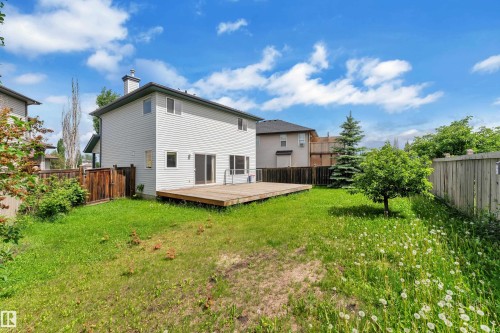 Expansive backyard featuring a large wooden deck, dual sliding glass doors, mature trees, and a wooden fence boundary - 14031 136 Street, Edmonton, AB 