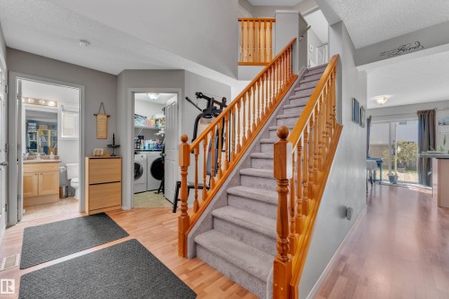 Split-level entry featuring wood-finish flooring, a carpeted staircase with wood banisters, and a light gray wall color - 14031 136 Street, Edmonton, AB 