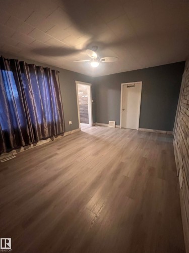 Spacious room featuring wood-finish flooring, dark accent walls, a ceiling fan with integrated lighting, and a stone-clad wall detail - 69 Railway Avenue, Star, AB 