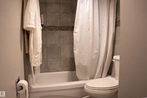 Tub and shower combination with full-height tile surround featuring a decorative mosaic accent band - 1703 11027 87 Avenue N, Edmonton, AB - Indoor Photo Showing Bathroom