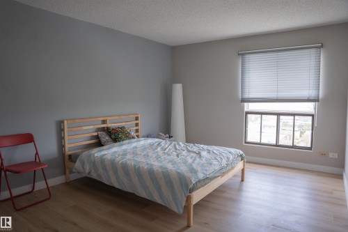 Spacious room with light wood-finish flooring, a neutral wall palette, and a large window with horizontal blinds - 1703 11027 87 Avenue N, Edmonton, AB - Indoor Photo Showing Bedroom
