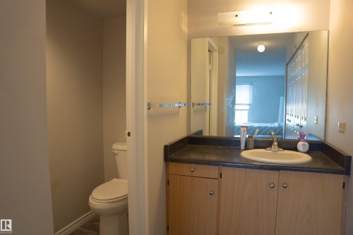 Bathroom featuring a vanity with wood-finish cabinetry, a dark countertop, an integrated sink, and an expansive wall-mounted mirror - 1703 11027 87 Avenue N, Edmonton, AB - Indoor Photo Showing Bathroom