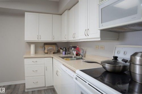 Kitchen featuring white cabinetry, light-toned countertops, a built-in microwave, and wood-finish flooring - 1703 11027 87 Avenue N, Edmonton, AB - Indoor Photo Showing Kitchen With Double Sink