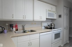 Kitchen featuring white cabinetry, light-toned countertops, a double basin stainless steel sink, an electric range, and an over-the-range microwave - 