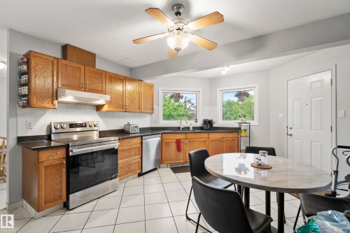 Kitchen featuring wood cabinetry, stainless steel appliances, dark countertops, and white tile flooring - 15503 62 Street, Edmonton, AB 