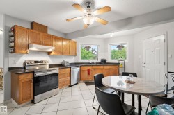 Kitchen featuring wood cabinetry, stainless steel appliances, dark countertops, and white tile flooring - 