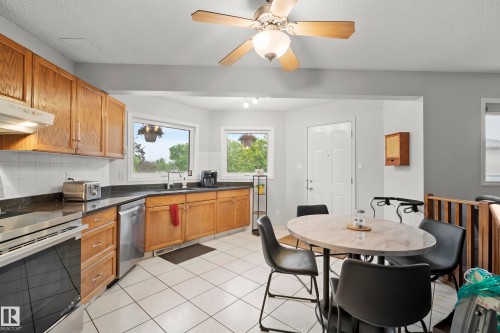 Kitchen featuring wood cabinetry, dark countertops, white tile backsplash, and stainless steel appliances including a range and dishwasher - 15503 62 Street, Edmonton, AB 