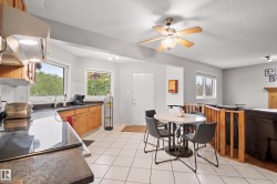 Open-concept kitchen and dining area featuring light wood cabinetry, dark countertops, white tile flooring, and a ceiling fan - 