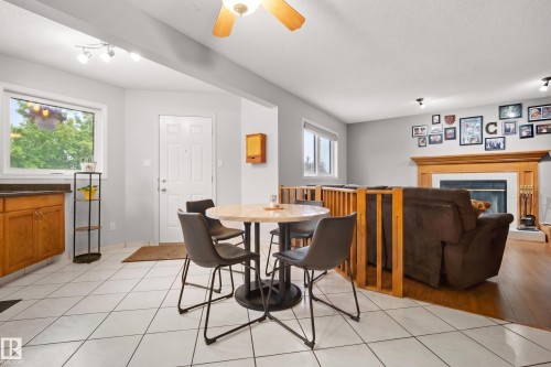 Bright open-concept space featuring white tile flooring, natural wood-finish cabinetry with dark countertops, and a white entry door - 15503 62 Street, Edmonton, AB 