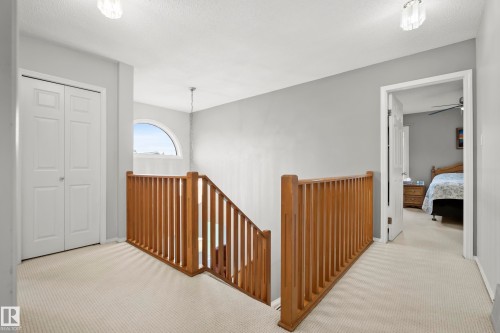 Upper level landing featuring light-toned carpeting, a wood railing, and an arched window - 15503 62 Street, Edmonton, AB 