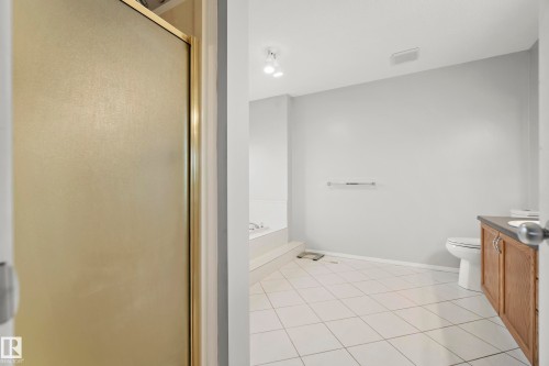 Spacious bathroom featuring a white tile floor, light gray walls, a built-in tub, and a vanity with a dark countertop and wood-finish cabinetry - 15503 62 Street, Edmonton, AB 