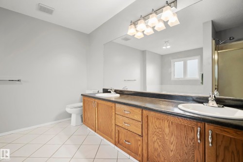 Bathroom featuring a double vanity with wood cabinetry, dark countertop, and integrated sinks - 15503 62 Street, Edmonton, AB 