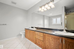 Bathroom featuring a double vanity with wood cabinetry, dark countertop, and integrated sinks - 