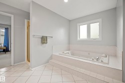 Soaking tub with tiled surround, single window, chrome fixtures, and a white tiled floor - 
