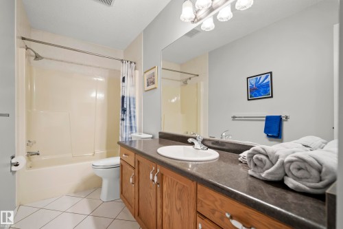 Full bathroom featuring a single vanity with a laminate countertop, undermount sink, and wood-finish cabinetry - 15503 62 Street, Edmonton, AB 