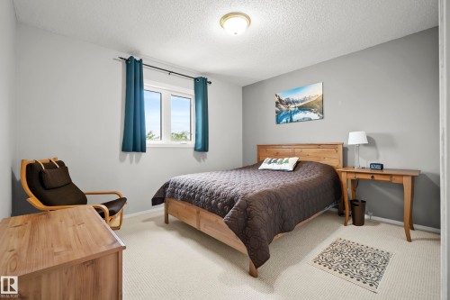 Carpeted room featuring a double window with dark blue curtains, light gray walls, and a textured ceiling - 15503 62 Street, Edmonton, AB 